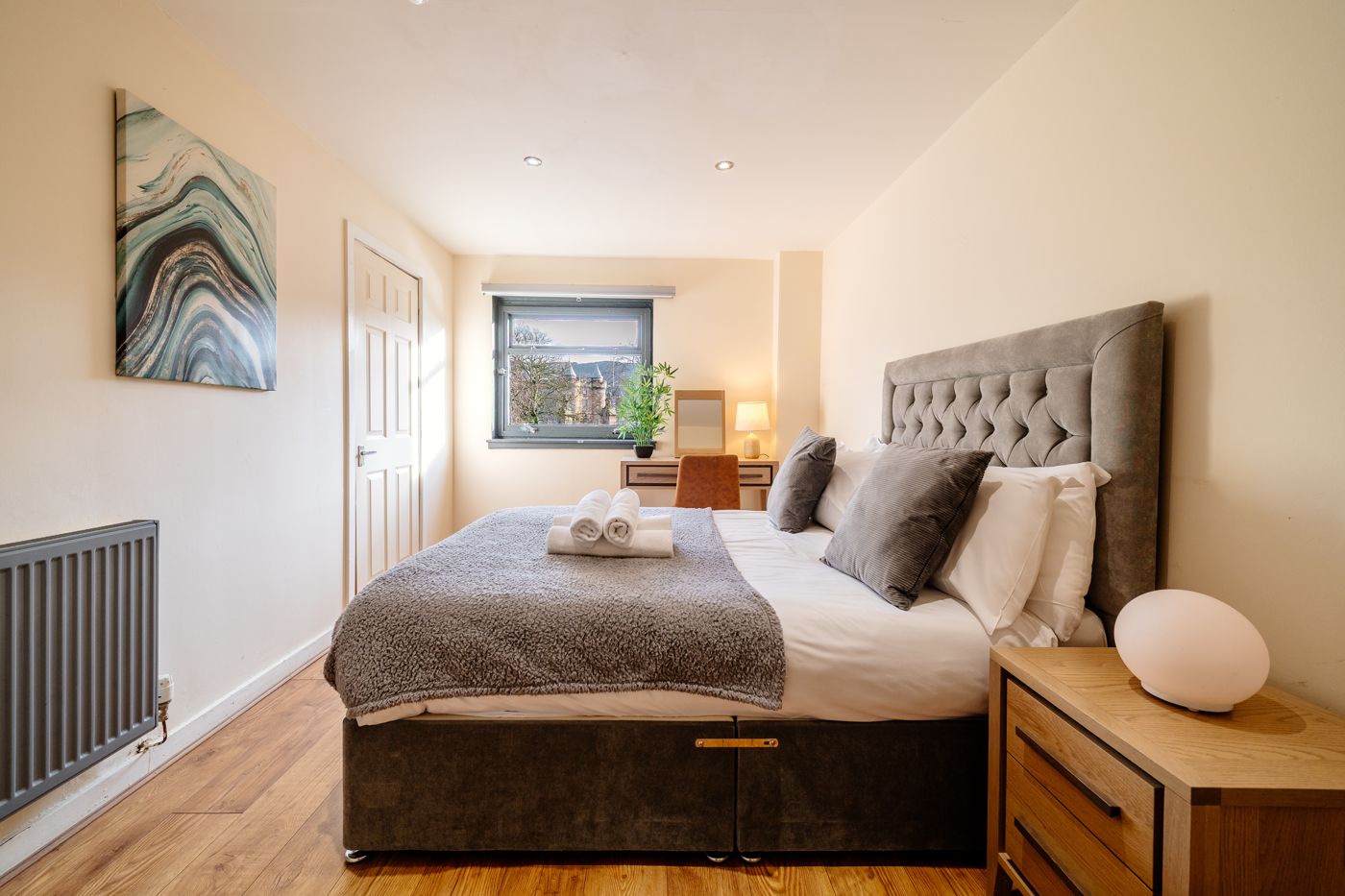 Double bedroom with a grey headboard, rolled towels and a desk by the window, in a home we look after in Abbeyhill