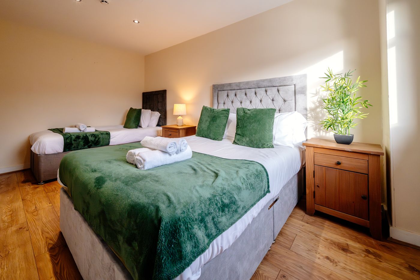 Bedroom with a double and a single bed, green throws and rolled towels, in Abbeyhill