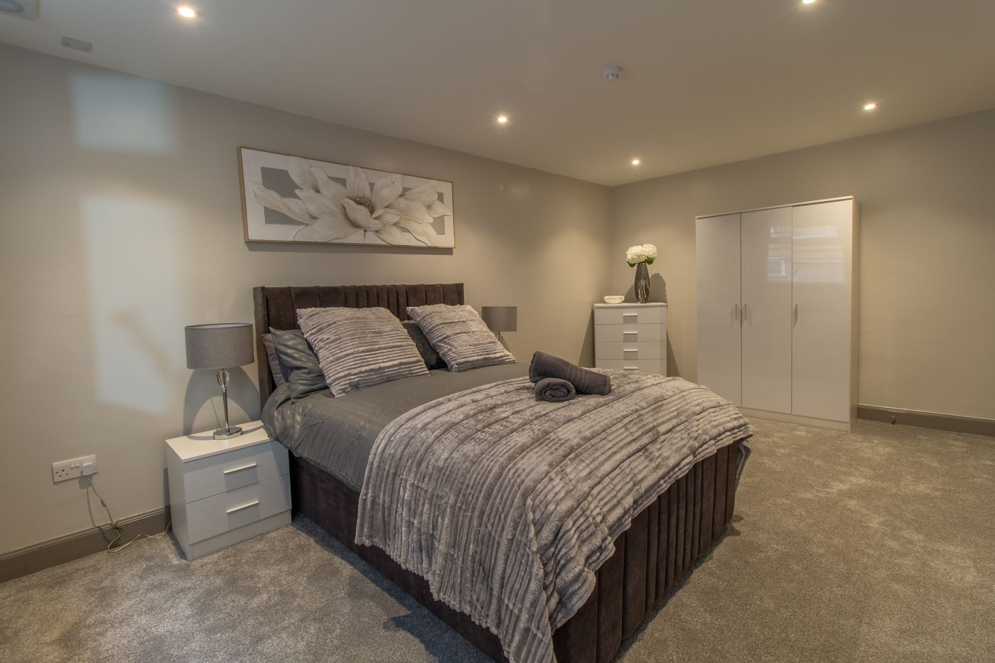 Large bedroom with a grey panelled bed and white wardrobes, in Dalkeith