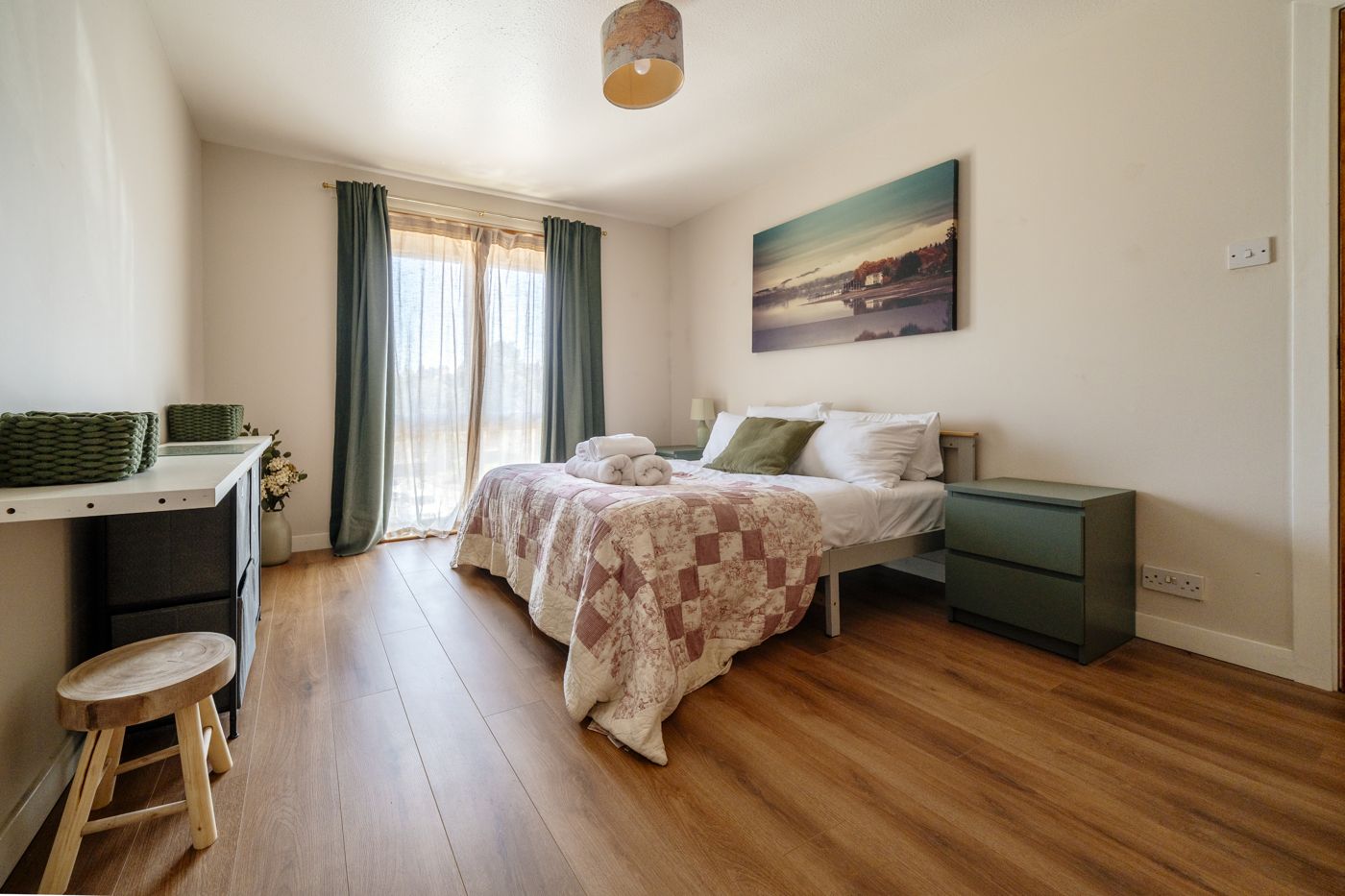 Double bedroom with green curtains, a patchwork quilt and rolled towels in a home we look after in Morningside