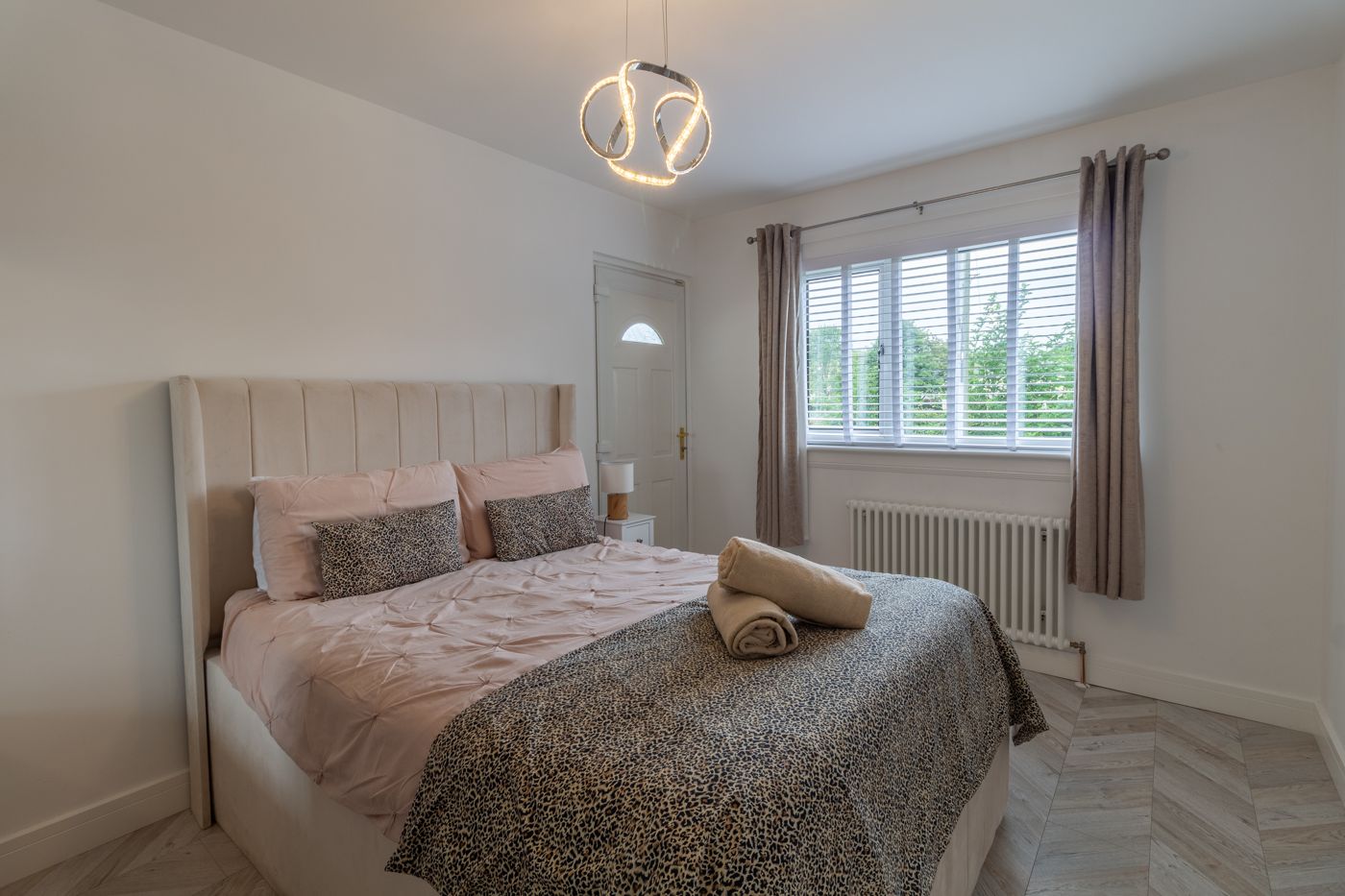 Double bedroom with a pale velvet headboard and rolled towels, in Prestonfield